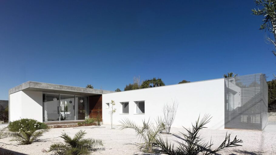 Los dos volúmenes blancos perpendiculares de la vivienda unifamiliar Elda con el acceso de madera.