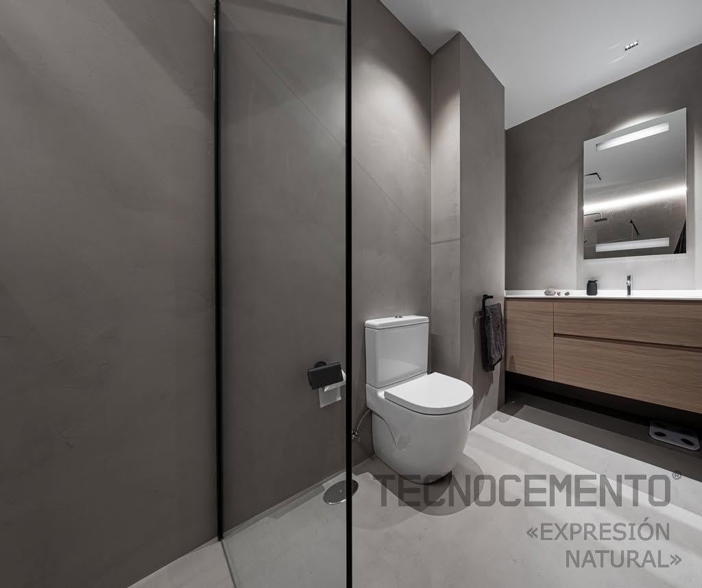 Salle d'eau en béton ciré gris avec paroi de douche vitrée, meuble vasque en chêne et miroir rétroéclairé